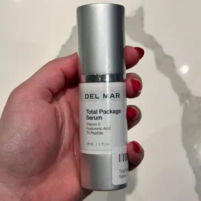 A person holding a bottle of DEL MAR Total Package Serum with Vitamin C and Hyaluronic Acid Tri-Peptide.